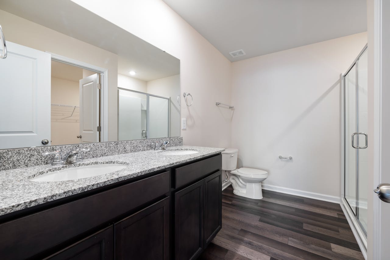 Elegant modern bathroom featuring granite countertops, glass shower, and hardwood floor for a sleek interior.
